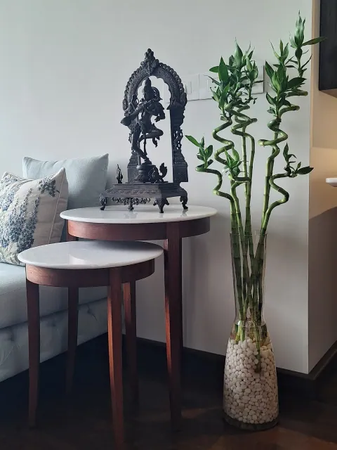 Lucky bamboo in a tall glass vase of white pebbles beside nesting marble side tables and a bronze idol, in a home in Oshiwara, Andheri West, Mumbai